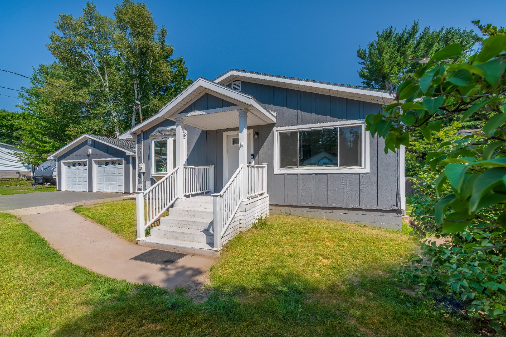 Street view of the finished gray board and batten house with covered porch, white railing, and detached two car garage in Marquette, MI