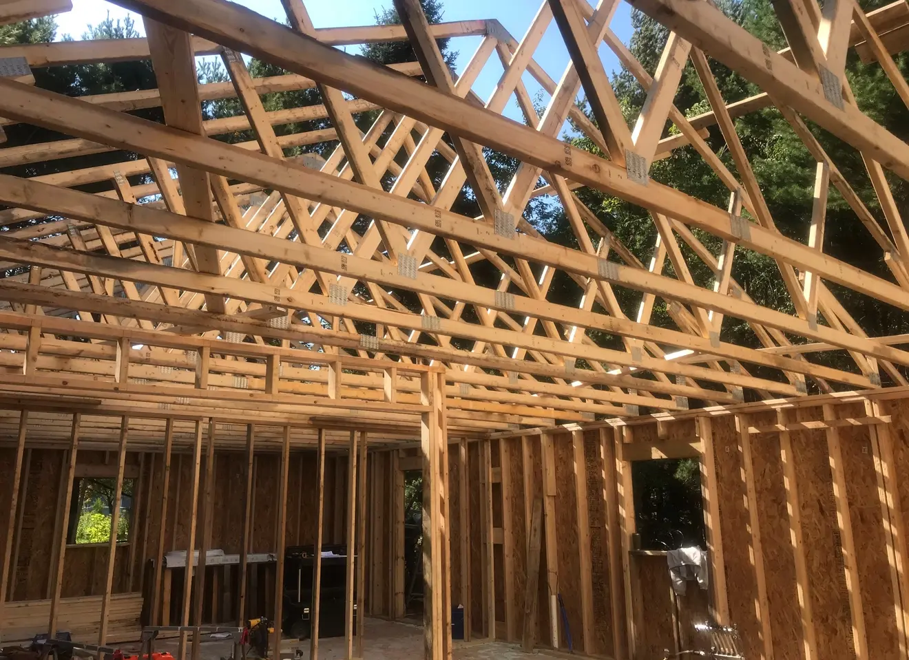 Interior view of new home framing with engineered roof trusses, wall studs, and OSB sheathing on a sunny day in Marquette, Michigan