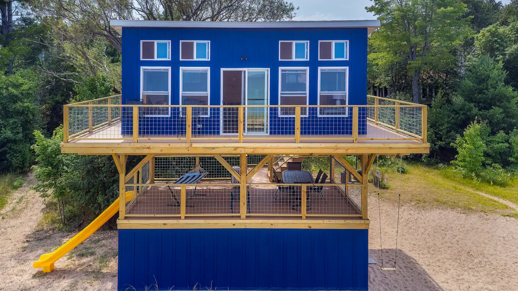 Custom multi-level deck with cedar railings and wire mesh panels on a blue modern home in Marquette, Michigan