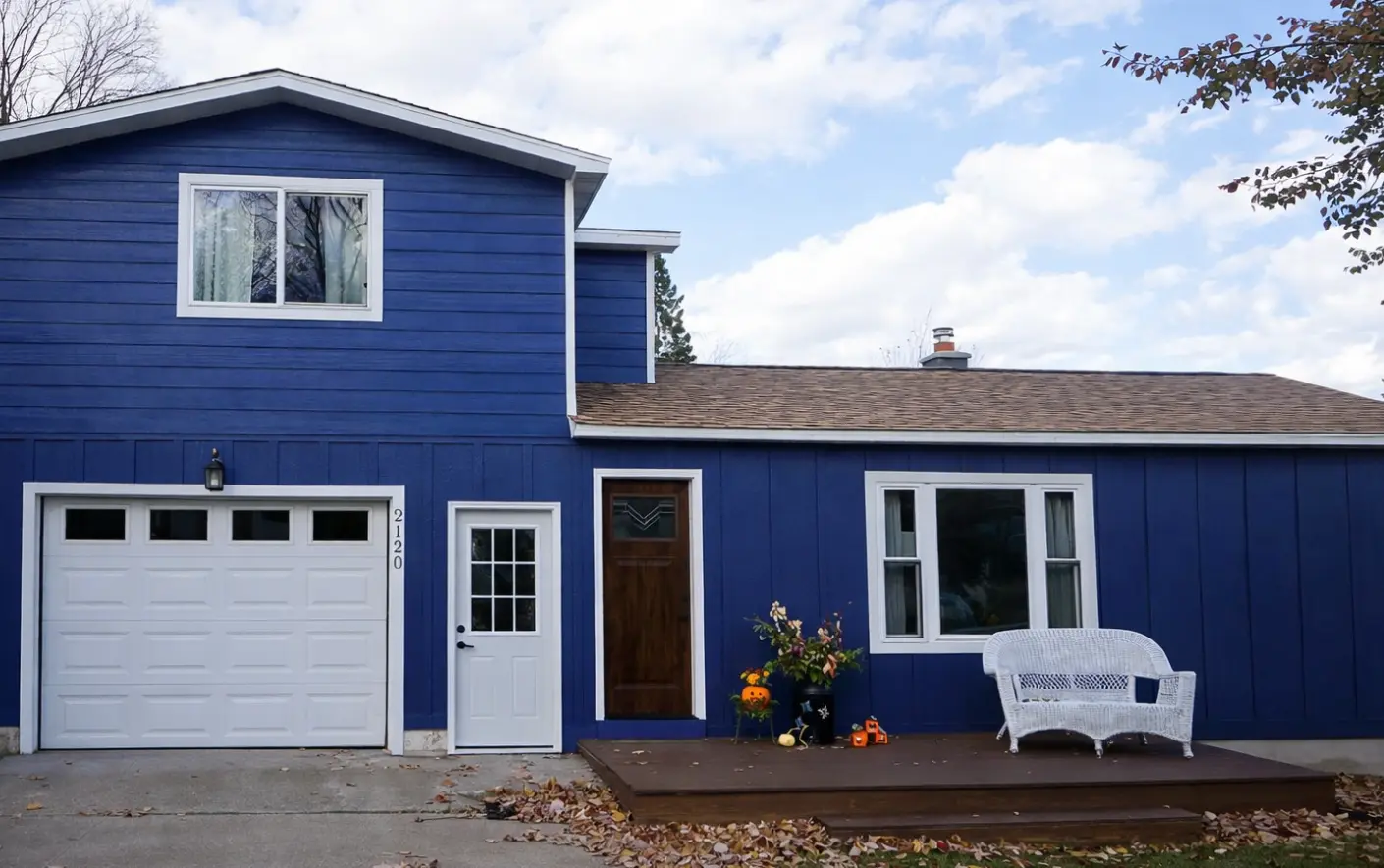 Completed siding installation with bold blue clapboard and board-and-batten siding, white trim, and wood front door on a Marquette, Michigan home